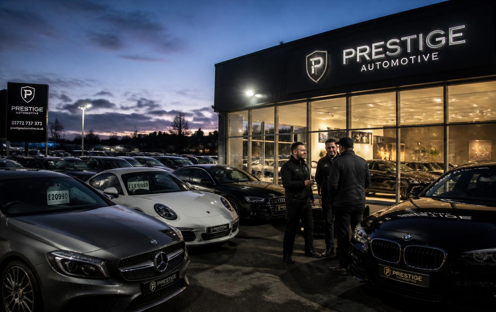 Dealership staff talking with a customer on an illuminated forecourt at dusk